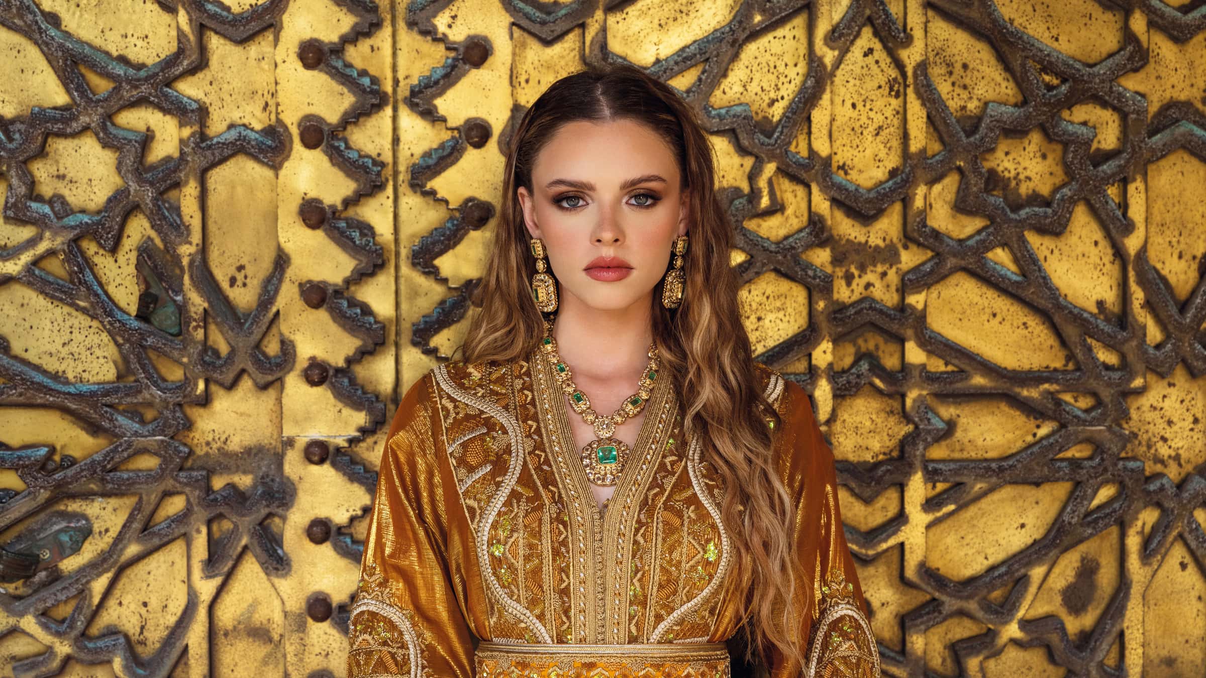 Caftan marocain doré de mariage brodé devant une porte marocaine ornée
